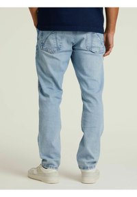 Vaqueros azul claro con un diseño de pierna recta, que cuentan con dos bolsillos traseros y un ligero desgaste; combinados con zapatillas blancas y una camisa oscura.