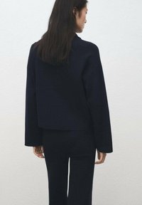 Námořnická krátká bunda se širokými rukávy, vyrobená z texturované látky. Disponuje boxovým střihem a minimalistickým designem.