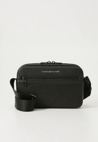 Musta olkalaukku, joka on valmistettu teksturoidusta synteettisestä materiaalista ja jossa on vetoketjutasku sekä säädettävä hihna. Etupuolella kohokuvioitu logo.