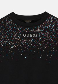 Maglione nero con strass multicolore attorno al collo e logo "GUESS" ricamato sul petto.
