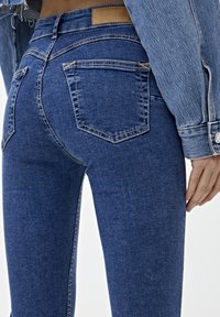 Jeans ajustados de denim azul con cintura alta, cinco bolsillos y costuras en contraste. Terminados con un parche de cuero en la parte posterior de la cintura.