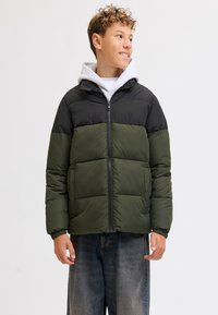 Kurtka puchowa z czarnym górnym fragmentem i oliwkowozielonym dolnym. Posiada zamek błyskawiczny i elastyczne mankiety, noszona na szarej bluzie z kapturem.