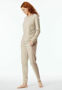 Beiges Loungewear-Set bestehend aus einem Langarmoberteil und gerippten Seitenpaneelen an der Hose. Der Stoff ist weich, mit einer lockeren Passform und einem schmal zulaufenden Design der Beine.