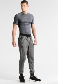 Grå tettsittende atletisk skjorte med en strukturert mønster, kombinert med smale grå joggebukser med elastisk midje og sidelommer.