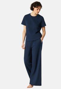 Navyblaues Loungewear-Set aus weichem Stoff, bestehend aus einem kurzärmeligen Oberteil und lockeren Hosen mit Seitentaschen und dezentem Logo-Detail.