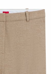 Beige stoffen broek met een textuurafwerking, voorzien van een standaard tailleband, riemlussen en zijzakken. Gevoerd interieur met een rode accentkleur.