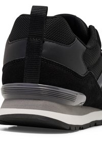 Sneaker nera con tomaia in mesh testurizzato, dettagli in suede e suola in gomma grigia con strisce bianche, dotata di un linguetta sul retro.