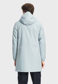 Un impermeabile azzurro chiaro impermeabile presenta un cappuccio, maniche lunghe e polsini elasticizzati. Ha un design di lunghezza media e una texture liscia.