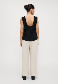 Top nero senza maniche con spalline arricciate e schiena scoperta. Abbinato a pantaloni larghi color crema e scarpe nere con tacco a blocco. Design minimalista.
