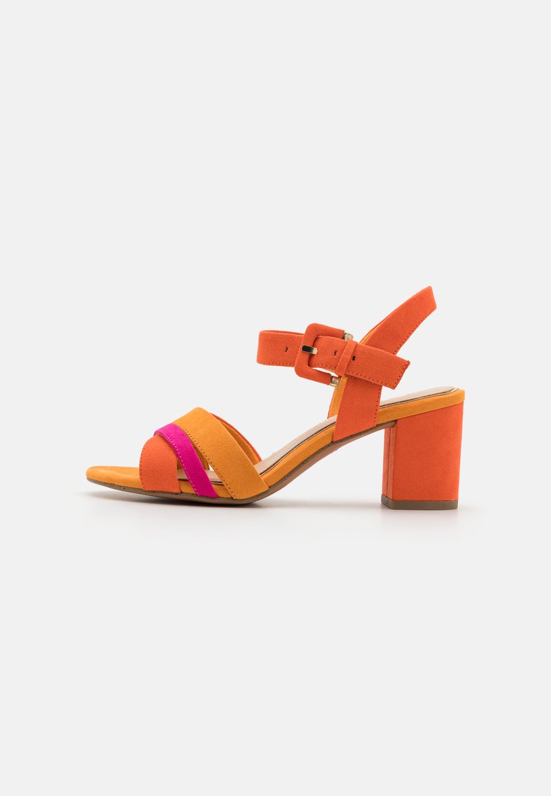 Sandale à talon en daim orange et rose avec un talon bloc, une bride de cheville avec une boucle, et des brides croisées sur le pied. Semelle plate.