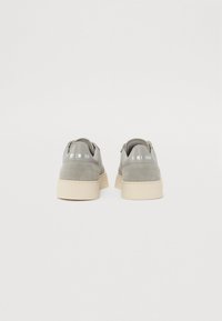Adidași gri din suede cu o talpă platformă bej, prezentând un bot rotund și brandul "Steve Madden" pe toc.