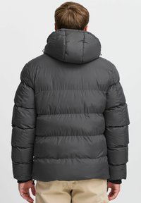 Polstret sort jakke med en justerbar hætte, der har vandret syninger, elastiske ærmer og et elegant design.