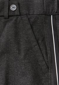 Tissu noir texturé avec fermeture à bouton, détails rayés verticaux et une poche avant. Surface lisse avec un léger éclat.