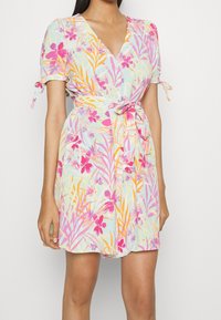 Kleid mit Blumenmuster, V-Ausschnitt, kurzen Puffärmeln und einem Bindegürtel. Die Farben umfassen Pastellrosa, Lila, Orange und Hellblau.