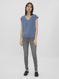 Blå V-hals kortermet t-skjorte kombinert med grå slim-fit jeans og svarte sko, satt mot en lys grå bakgrunn.