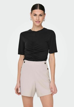 Top negro de manga corta con detalles fruncidos en la parte frontal, combinado con pantalones cortos de talle alto en color rosa claro que presentan acentos de botones dorados en los laterales.