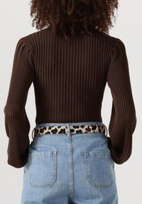 Braunes geripptes langärmeliges Oberteil mit figurbetontem Schnitt, kombiniert mit hochgeschnittenen blauen Jeans und einem Gürtel im Leopardenmuster.