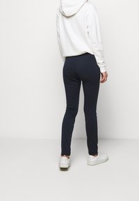 Leggings navy au contour ajusté, fabriqués en matière extensible, associés à un sweat à capuche blanc et des baskets blanches.