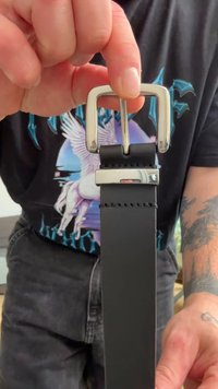 Musta nahkavyö, jossa on hopeanvärinen suorakaiteen muotoinen solki, sileä pinta ja näkyvät ompelut.