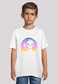 Weißes Baumwoll-T-Shirt mit einem retro-alien Grafik und dem Text "I COME IN PEACE" in Gelb, vor einem mehrfarbigen gestreiften Hintergrund.