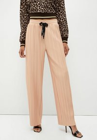 Pantaloni plissettati pesco con vita alta, cintura elastica e dettaglio in raso nero. Il tessuto ha una consistenza liscia con un design a gamba larga.