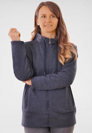 Sweat à zip gris foncé avec un col haut, doté de cordons de serrage, de poches latérales et d'une doublure intérieure texturée. Tissu doux avec une coupe décontractée.
