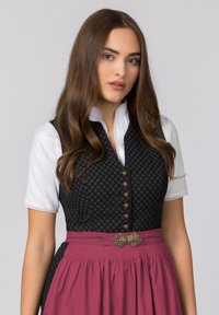 Traditionelles Kleid mit einer dunklen gemusterten Weste, einer weißen Bluse und einem langen rosa Rock mit einer dekorativen Schnalle.