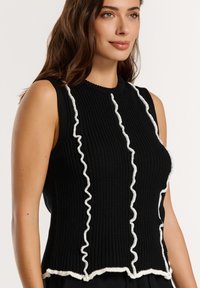 Mustad must õmblusteta topp, mis on varustatud valgete volangidega ääred õmbluste ümber ja ribakaelusega, ümmarguse kaeluse ja laieneva servaga.