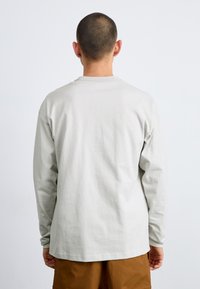 Cămașă lungă cu mâneci, gri deschis, realizată dintr-un material moale, având un guler rotund și o croială lejeră. Vedere din spate care evidențiază un design simplu, fără grafică.