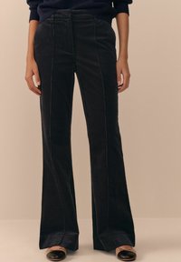 Black corduroy flared pants with vertical seams, featuring a high waist and smooth texture, paired with black flats.