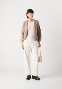 Pehme beige kardigan, sobiv valge topp, laiad valged püksid tekstuurse viimistlusega ja muljetavaldavad mustad platvormijalatsid. Käes minimalistlik käekott.
