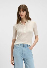 Polo shirt a coste di un beige chiaro con maniche corte, dotato di colletto e chiusura con bottoni, abbinato a jeans di denim blu chiaro.