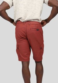 Shorts cargo rouges avec une texture lisse, poches latérales et une poche arrière. Présente une fermeture à bouton et une étiquette logo à l'arrière.