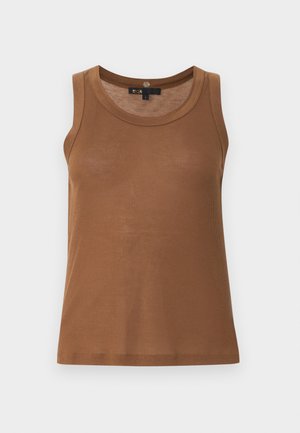 Naine kannab pruuni varrukateta topi ja laia säärega siniseid teksapükse väikeste mustritega, hoiab hõbedast käekotti ja kannab musti kontsakingi.