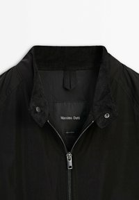 Veste noire avec col en velours côtelé, fermeture éclair en métal et boutons-pression, montrant l'étiquette "Massimo Dutti" à l'intérieur du col.