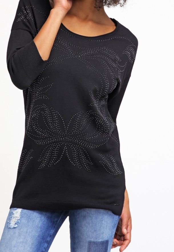 Felpa nera con scollo a barca, motivo decorativo di strass e maniche a tre quarti, abbinata a jeans blu strappati.