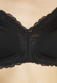 Black bralette featuring lace trim along the neckline and edges, with a smooth fabric base and a central clasp detail for support.