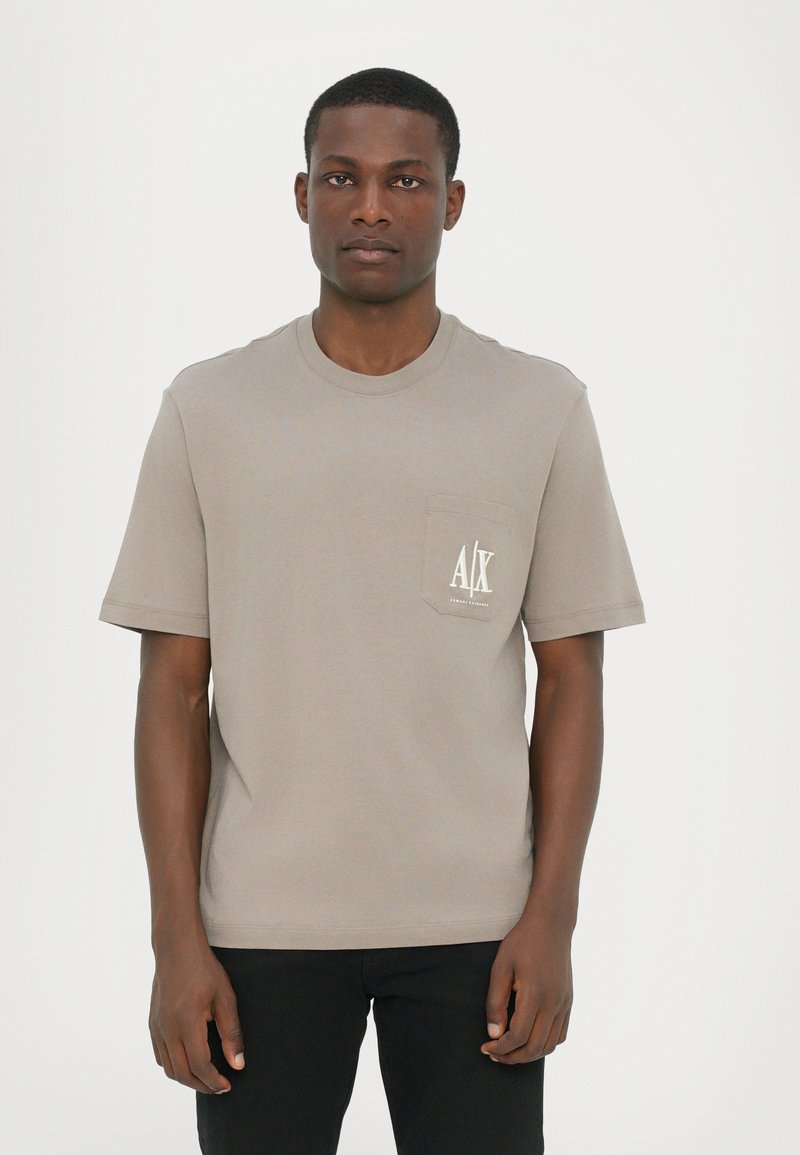 T-shirt a maniche corte, con collo rotondo, in una tonalità beige tenue. Presenta una tasca sul petto con un logo stampato. Tessuto morbido con una superficie liscia.