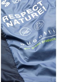 Dunkelblauer Stoff mit weißen und grünen Texten und Symbolen, die Nachhaltigkeit fördern. Der Text beinhaltet "RESPEKTIERE DIE NATUR!" und den Markennamen "bugatti."