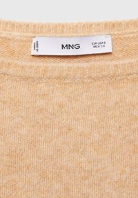 Beige Strickpullover mit Rundhalsausschnitt und weicher Textur. Das Pflegeetikett zeigt "MNG" und die Größenangaben. Hergestellt in China.