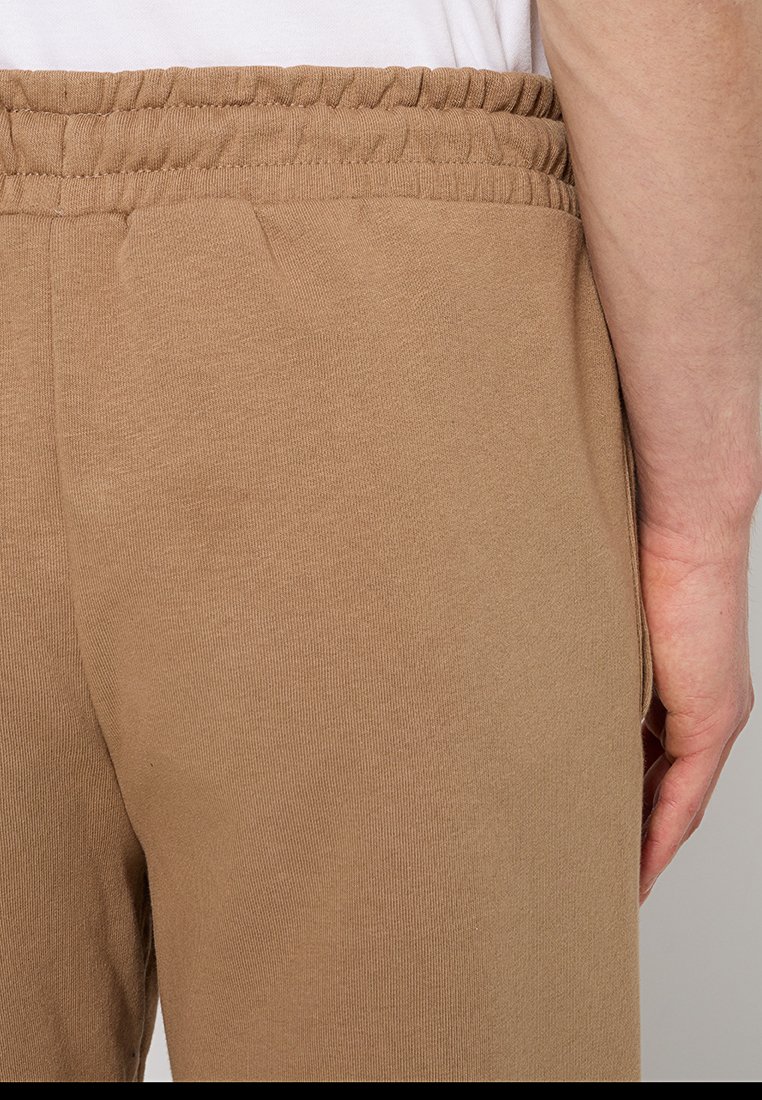 Jogger beige con cintura elastica; realizzati in tessuto morbido e stretchy. Presentano una texture liscia e una tasca laterale.