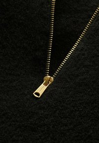 Svart texturerad tyg med guldblixtlåsdetalj som är delvis öppen, med en slät dragkedja och tänder för säker stängning.