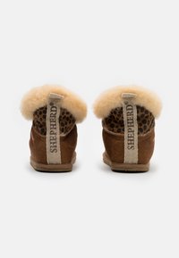 Brown suede slippers with a fluffy cream lining, a textured animal print interior, and a woven fabric pull tab at the back.