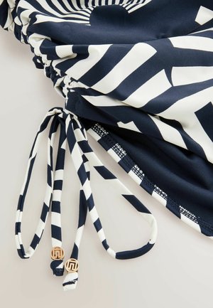 Marineblå og hvid mønstret badetøj med snorelukning, der har kontrasterende striber og gyldne detaljer på snorens ender.