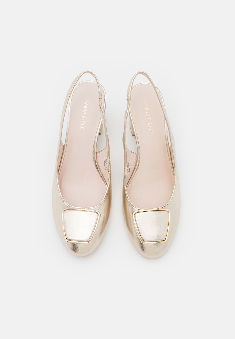 Ballerines slingback métalliques dorées présentant un bout carré avec un accent brillant. Texture lisse avec des côtés ouverts pour une ventilation.