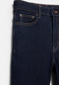 Jeans din denim de culoare albastru închis, cu un design clasic cu cinci buzunare, cusături în contrast și o croială dreaptă. Materialul prezintă o textură subtilă.