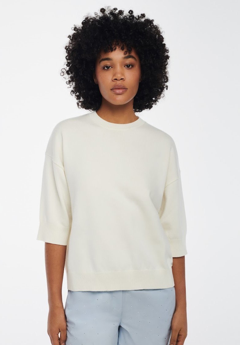 Maglione oversize beige chiaro a maglia con maniche corte e dettagli a costine nei polsini e nell'orlo. Texture liscia, vestibilità casual, design minimalista.