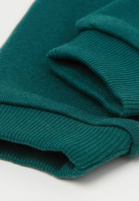 Tyrkysová ribová pletenina složená tak, aby byla vidět textura a vrstvené okraje na světlém pozadí.