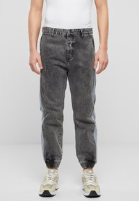 Joggers de denim de talle alto con un lavado negro desgastado, detalles en paneles laterales de color azul claro y puños elásticos. Combinados con zapatillas en tonos neutros.