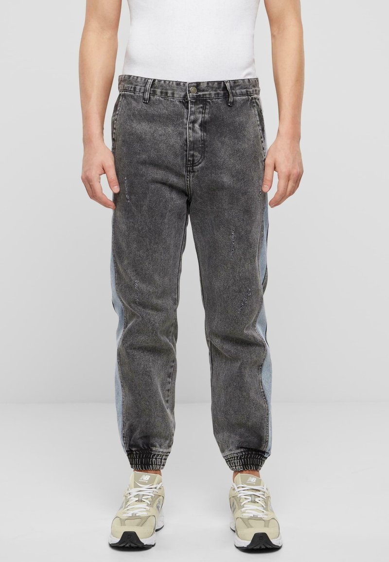 Joggers de denim de talle alto con un lavado negro desgastado, detalles en paneles laterales de color azul claro y puños elásticos. Combinados con zapatillas en tonos neutros.